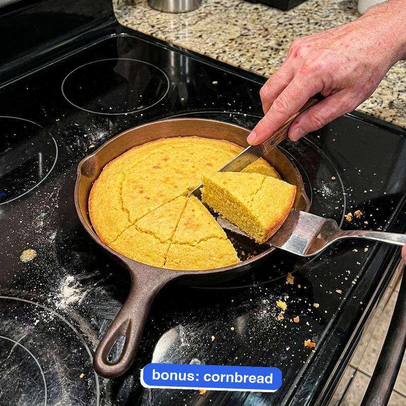 Cornbread sliced into wedges in the bronze-interior iLume on a flour-dusted cooktop, one wedge lifted out on a spatula.